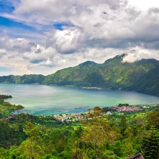Panoramic view of a lake surrounded by mountain, tropical landscape with colorful clouds in the sky. Fisheries and settlements on the shore.